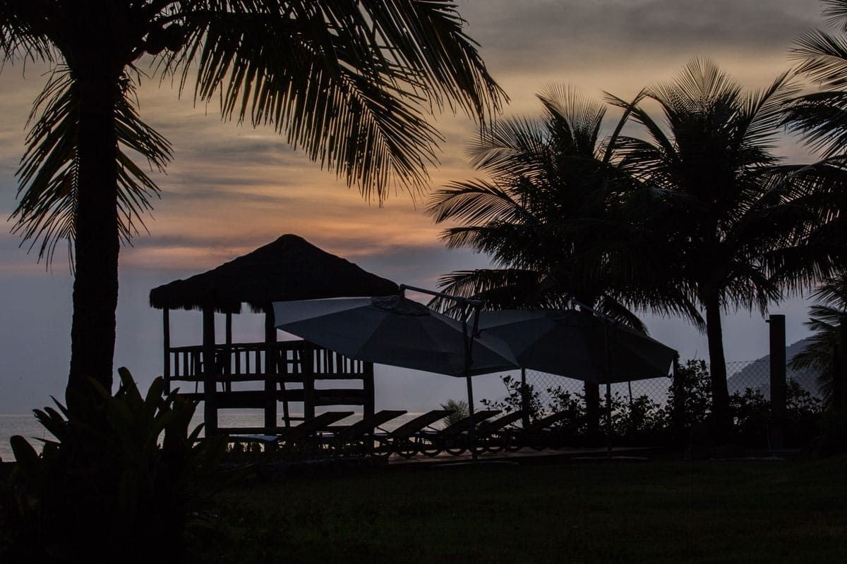 Uma silhueta de uma cabana com guarda-sóis e palmeiras ao pôr do sol