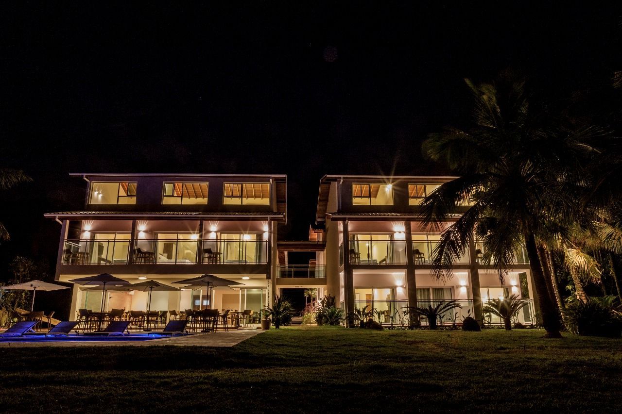 Uma casa grande é iluminada à noite com uma piscina na frente.