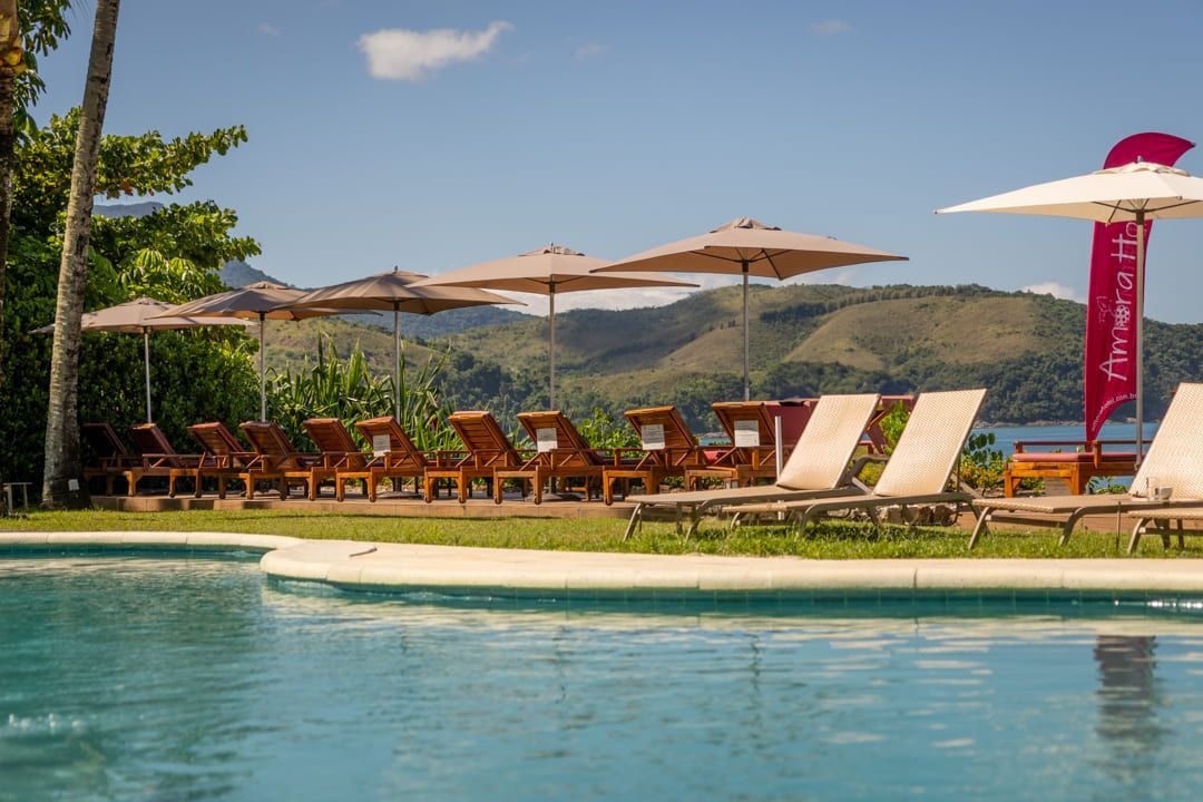 Uma piscina cercada por cadeiras e guarda-sóis com montanhas ao fundo.