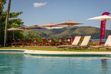 Uma piscina cercada por cadeiras e guarda-sóis com montanhas ao fundo.
