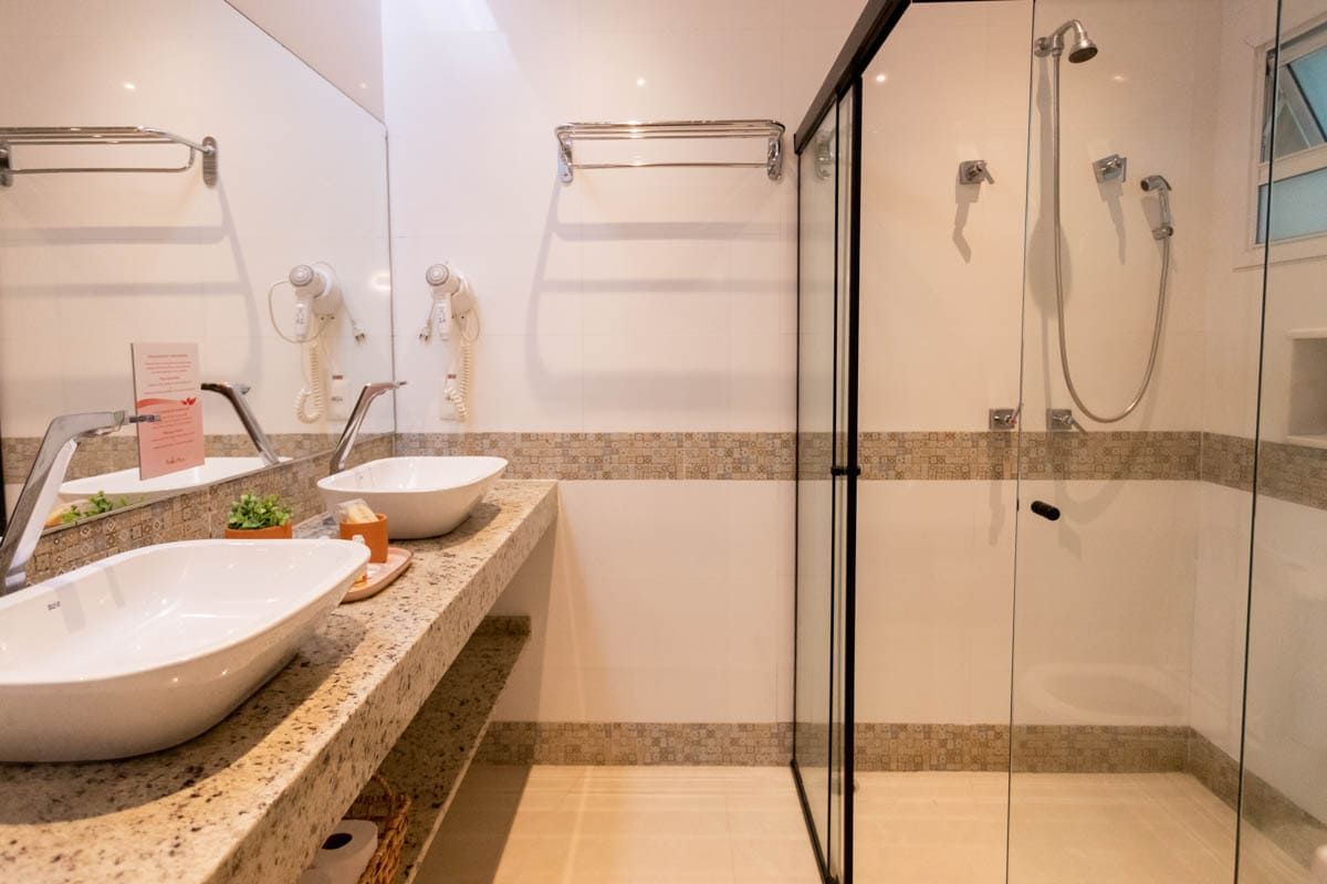 Um banheiro com duas pias, um chuveiro e um espelho.