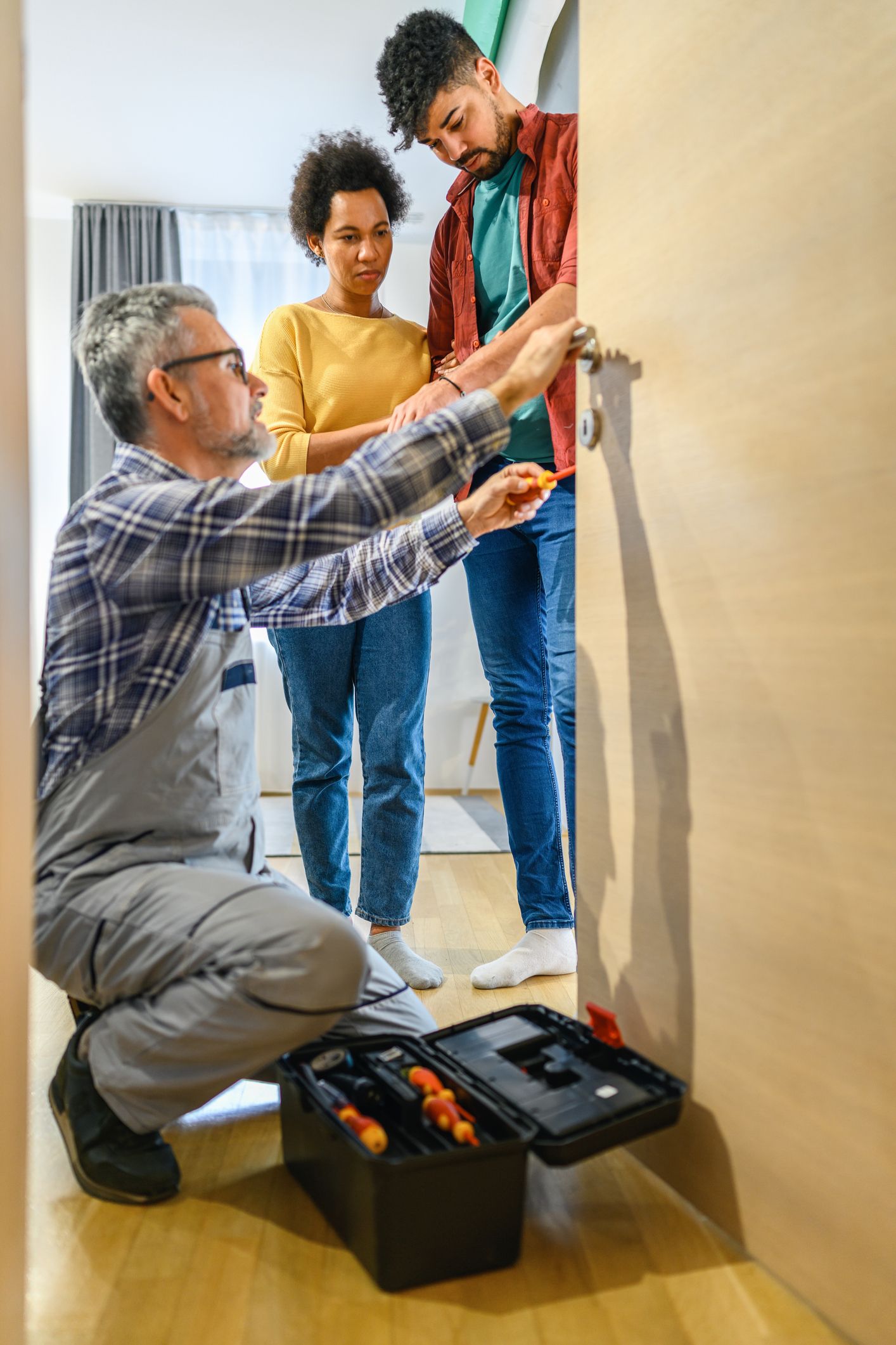 Locksmith repairing a house door lock with a screwdriver, offering residential locksmith services.