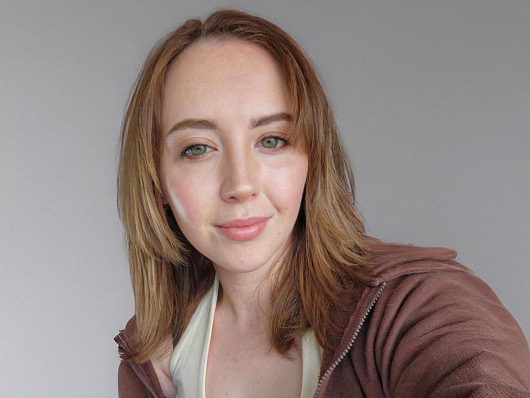 A woman in a brown jacket is taking a selfie.