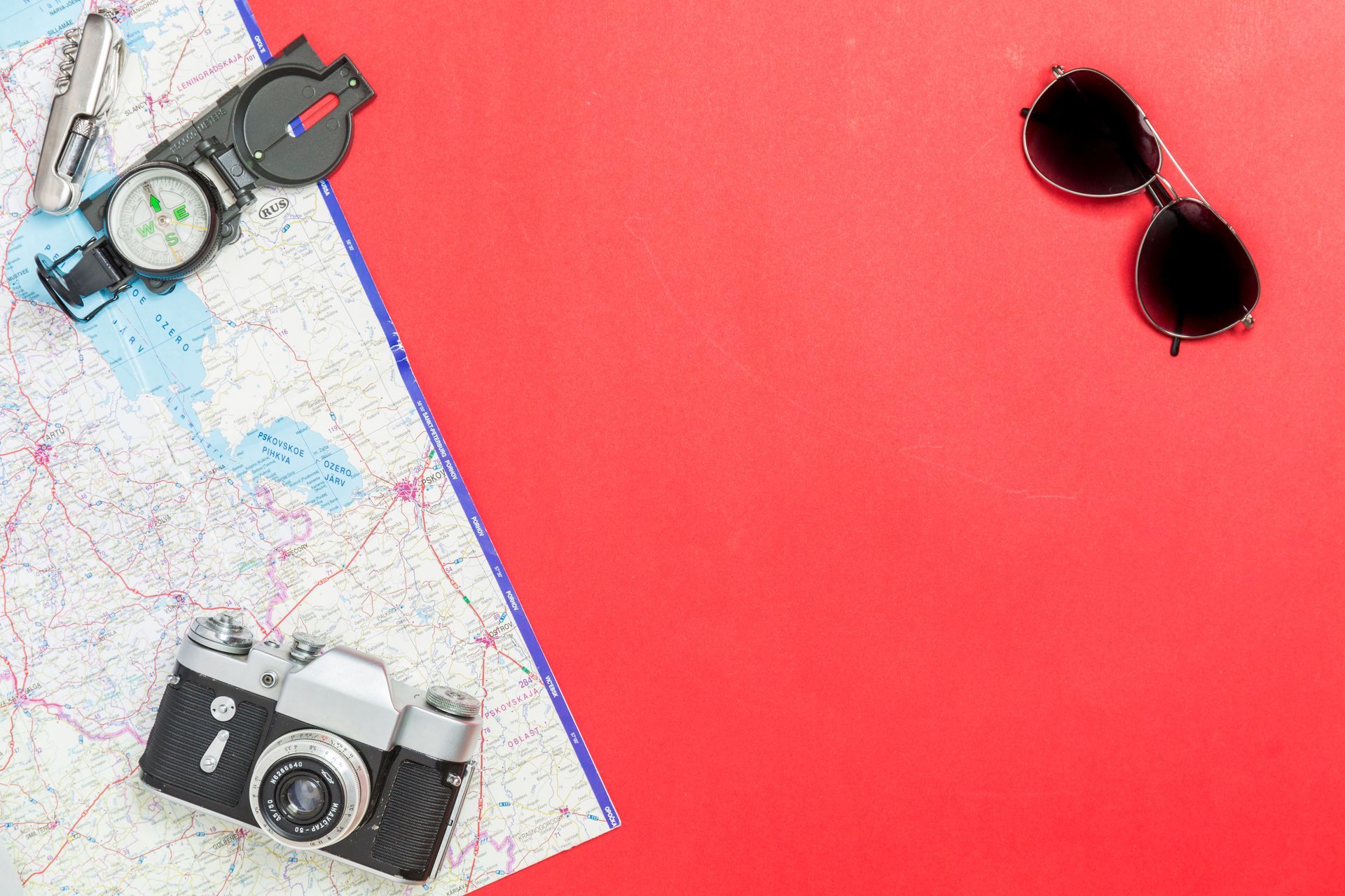 A camera , sunglasses , compass , watch and a map on a red background.