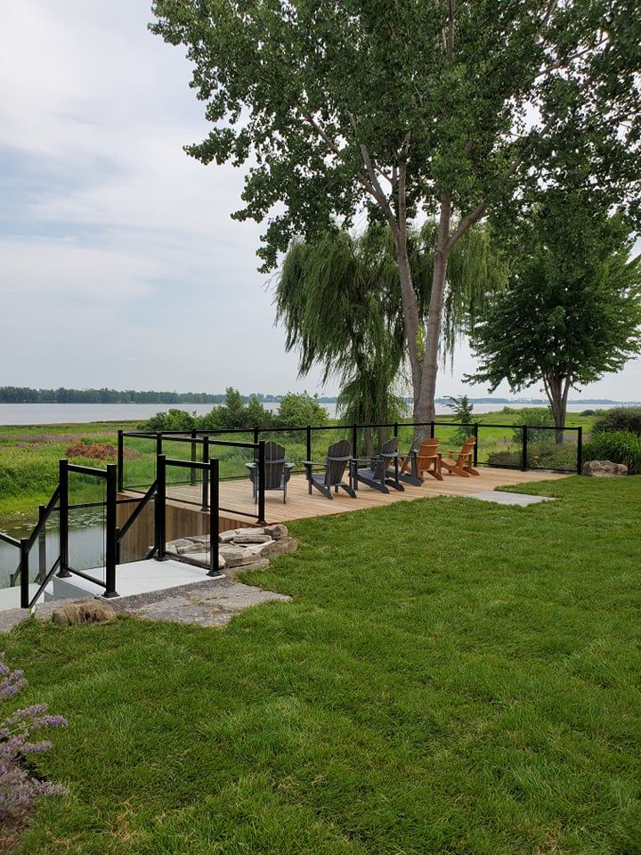 Une grande pelouse avec une terrasse et des chaises donnant sur un lac.