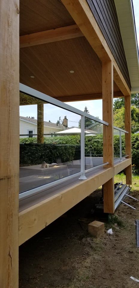 Une terrasse en bois avec une balustrade en verre est en cours de construction sur le côté d'une maison.