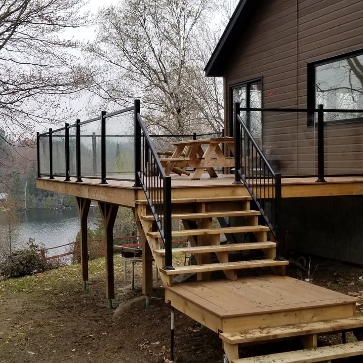 Une terrasse en bois avec des escaliers et une balustrade en verre à côté d'une maison.