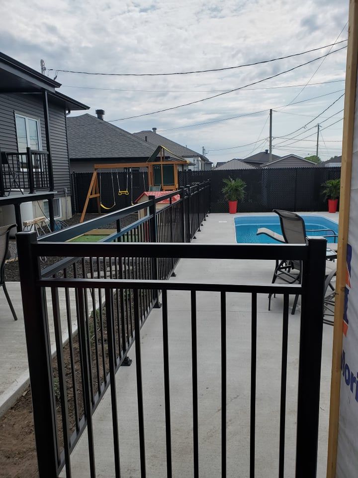 Une clôture noire entoure une piscine dans une cour arrière.
