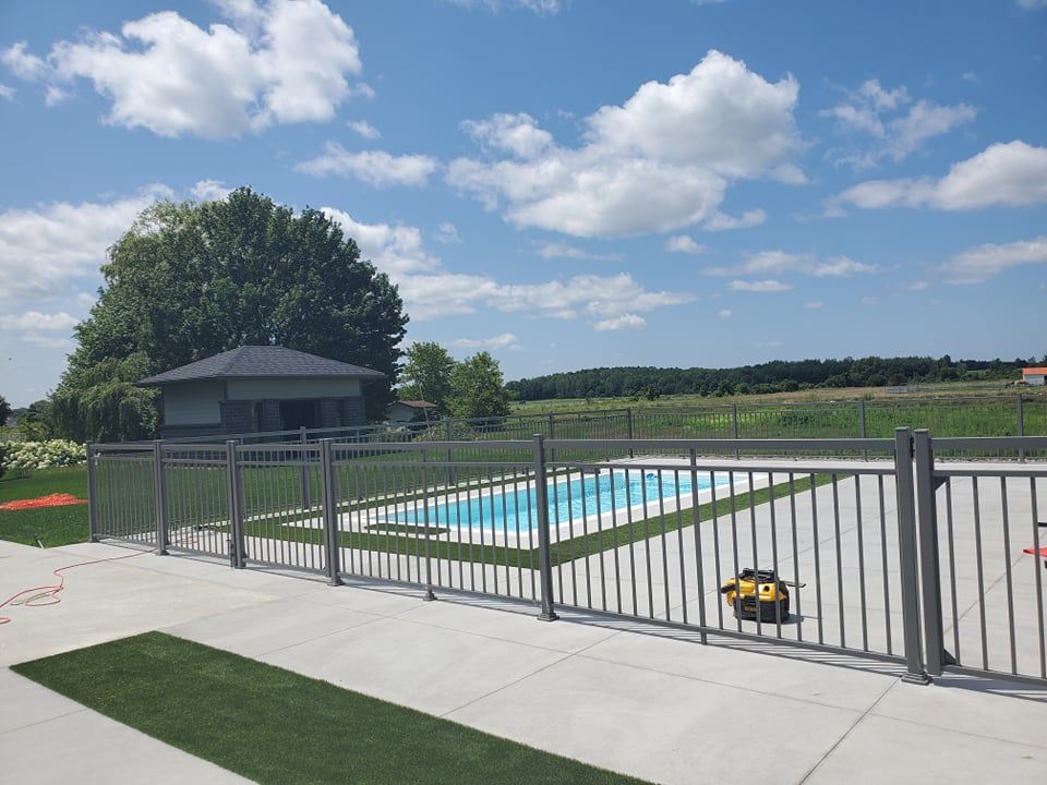 Une clôture entoure une piscine avec une maison en arrière-plan.