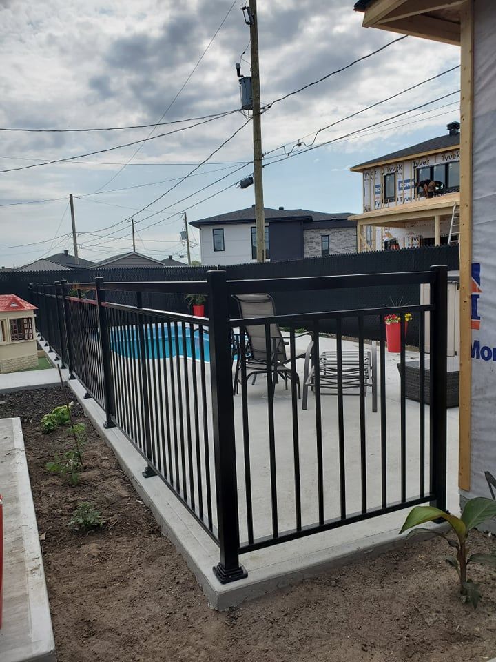 Une clôture en métal noir entoure une piscine dans une cour arrière.