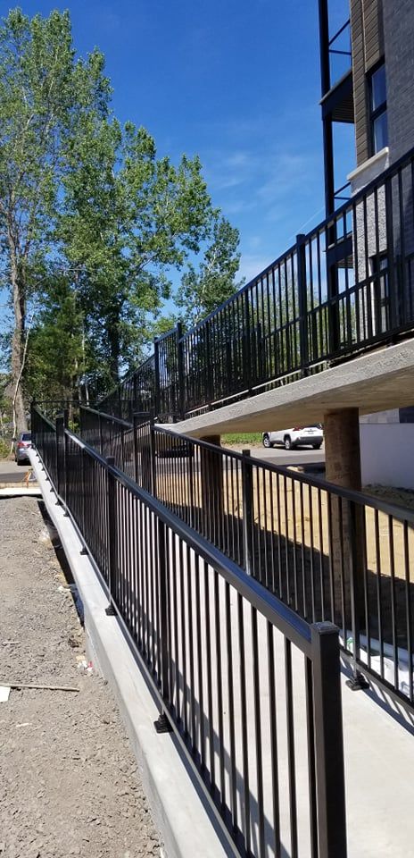 Une clôture en métal noir entoure une allée menant à un bâtiment.