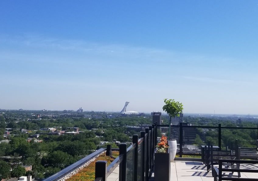 Un balcon avec vue sur une ville et des arbres par une journée ensoleillée.