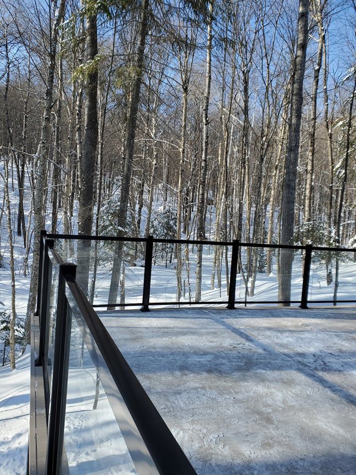 Une terrasse avec une balustrade en verre donnant sur une forêt enneigée.