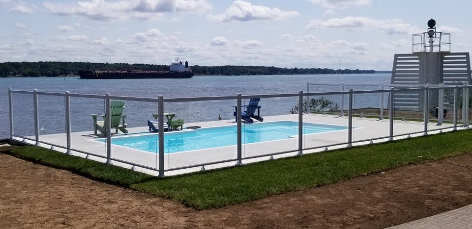 Une grande piscine entourée d'une clôture en verre surplombant un plan d'eau.