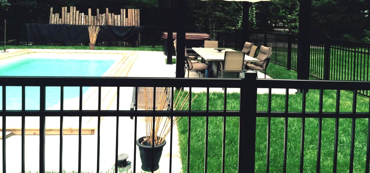 Jardin avec piscine, mobilier de jardin et clôture noire. Entouré d'une pelouse verdoyante et d'arbres luxuriants.