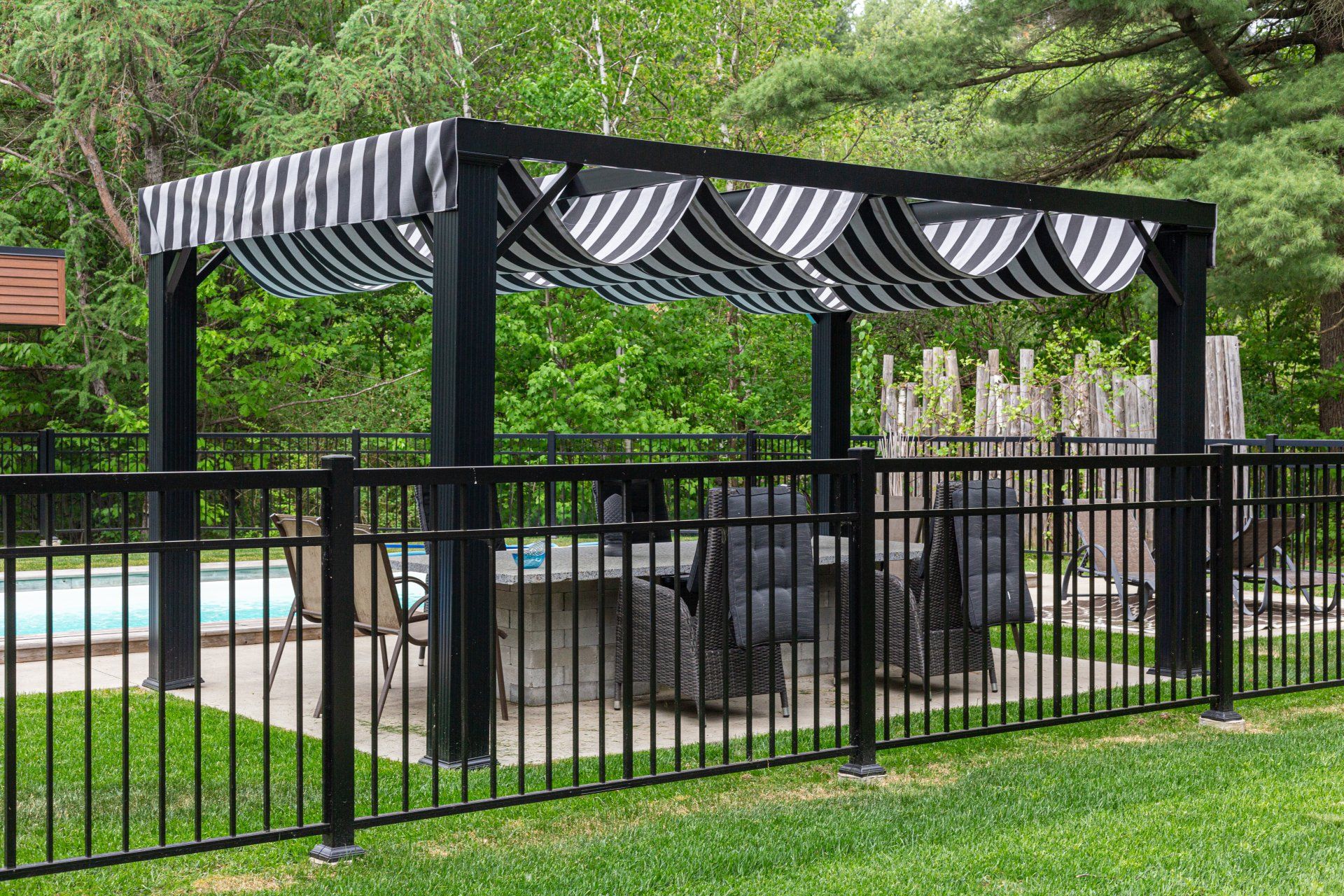 Une pergola rayée noire et blanche est assise à côté d'une piscine.