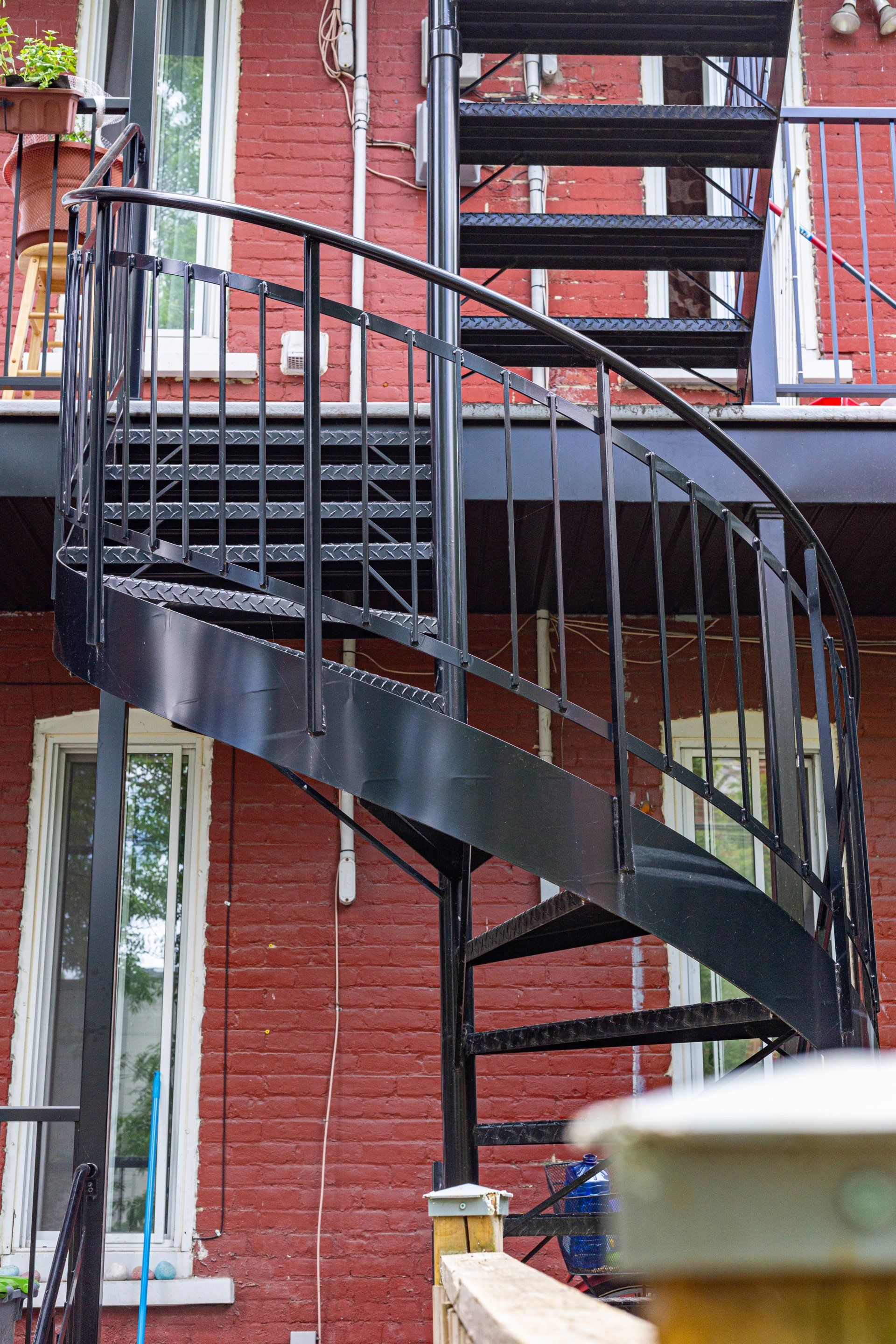 Un escalier en colimaçon noir se trouve à l'extérieur d'un bâtiment en briques rouges.