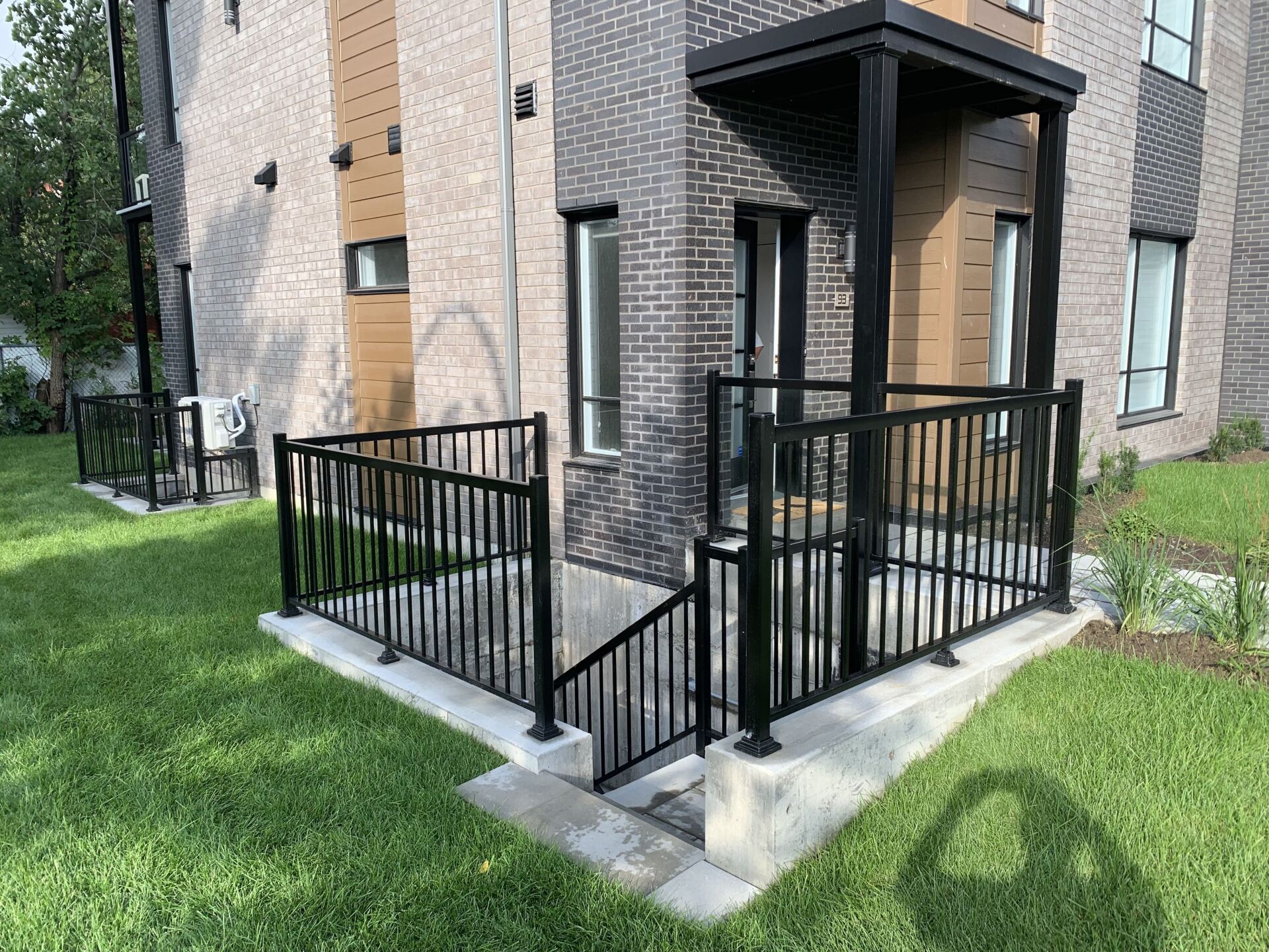 Entrée extérieure du bâtiment avec rambarde en métal noir, escaliers en béton et pelouse.