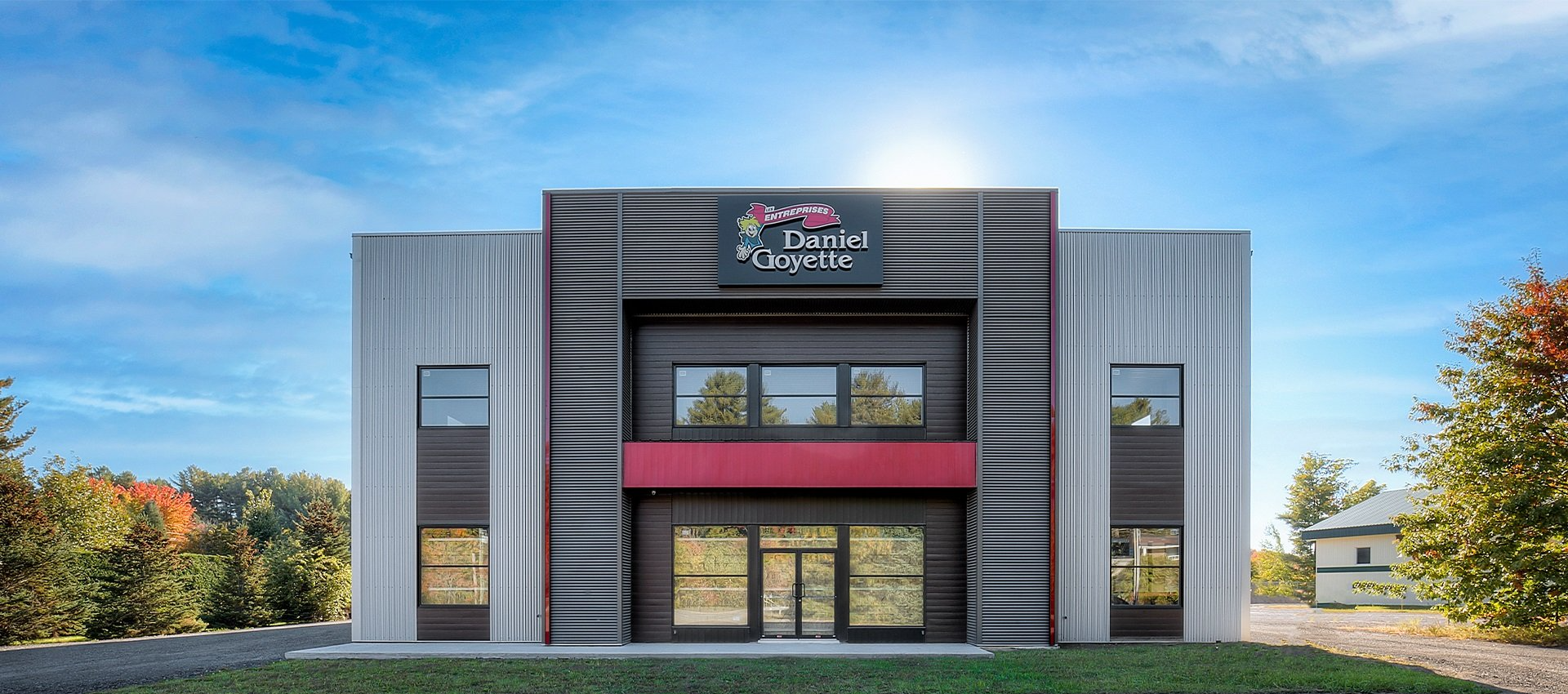 Un grand bâtiment avec un auvent rouge est entouré d'arbres et d'herbe.