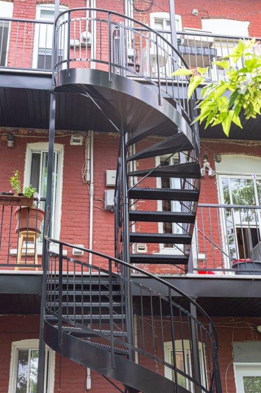Un escalier en colimaçon noir se trouve à l'extérieur d'un bâtiment en briques rouges