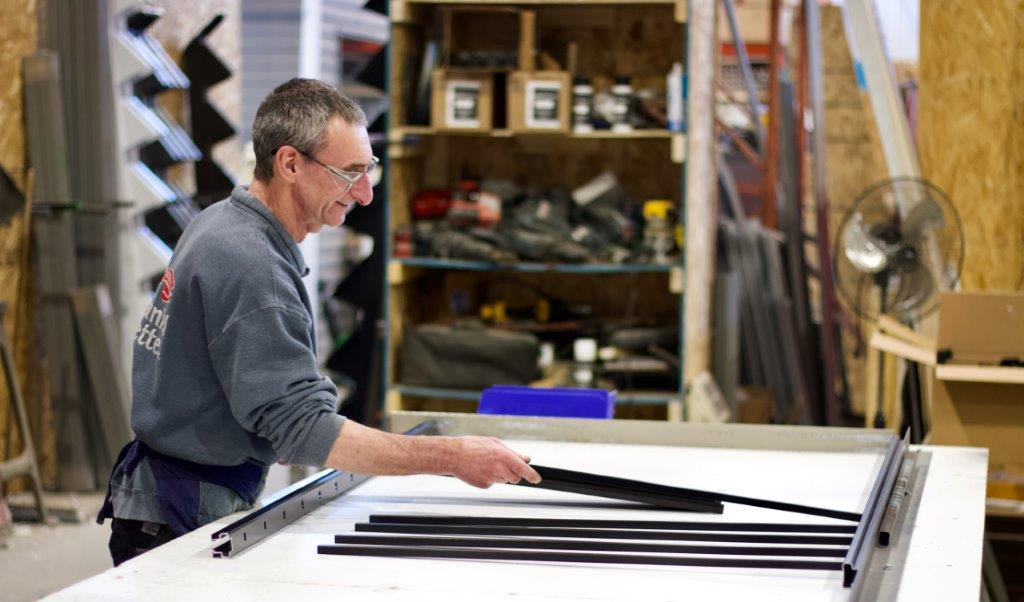 Un homme assemble des cadres de fenêtres noirs sur une table blanche dans un atelier.