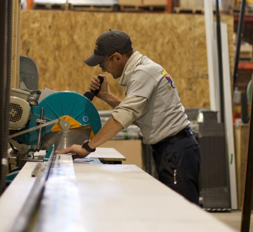 Un homme portant une casquette coupe du bois avec une scie électrique dans un entrepôt.