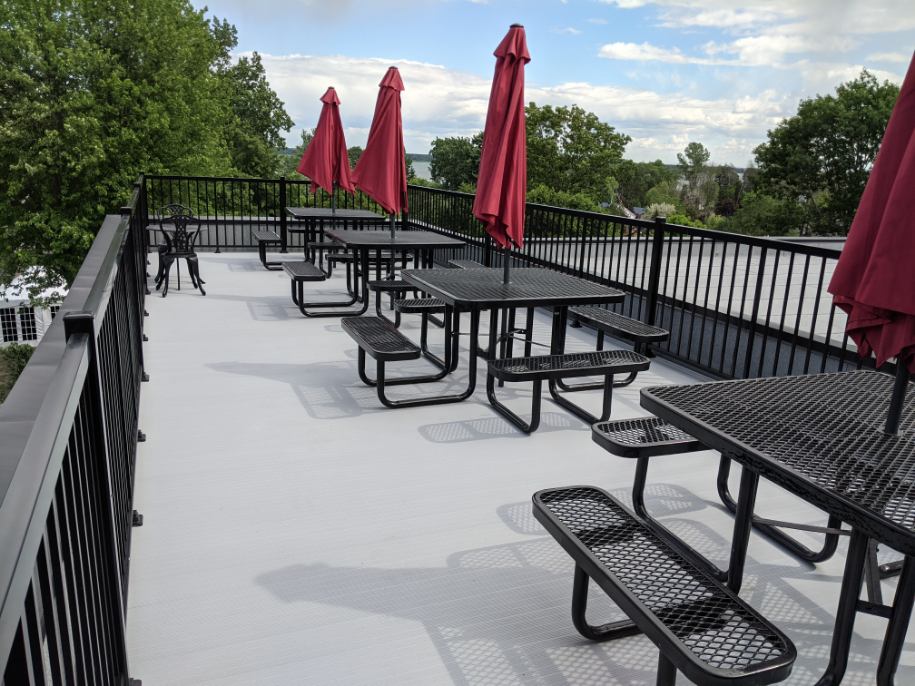 Une rangée de tables de pique-nique avec des parasols rouges sur un balcon.