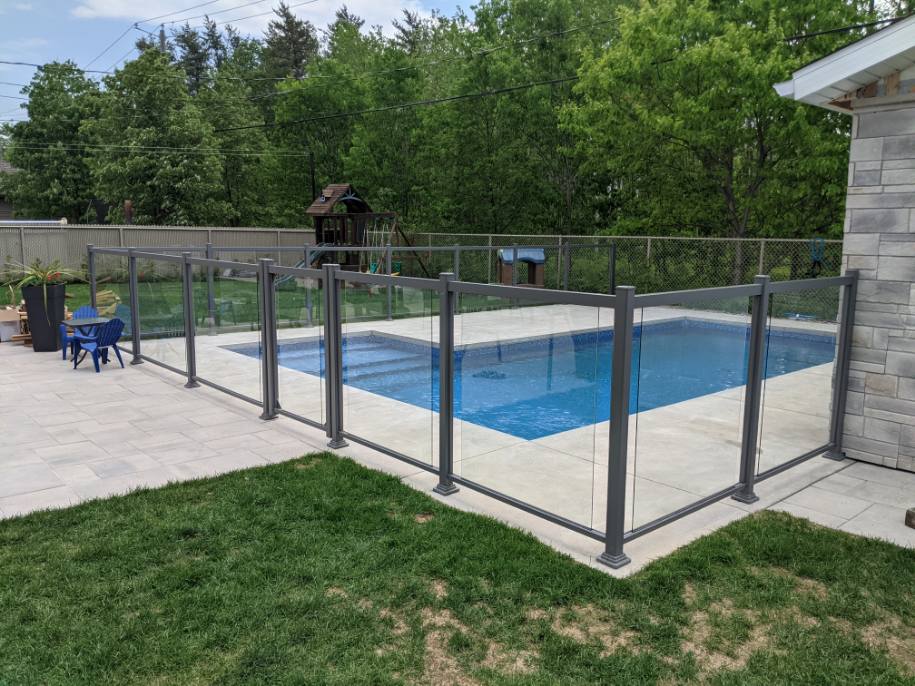 Une grande piscine entourée d'une clôture en verre dans une cour arrière.
