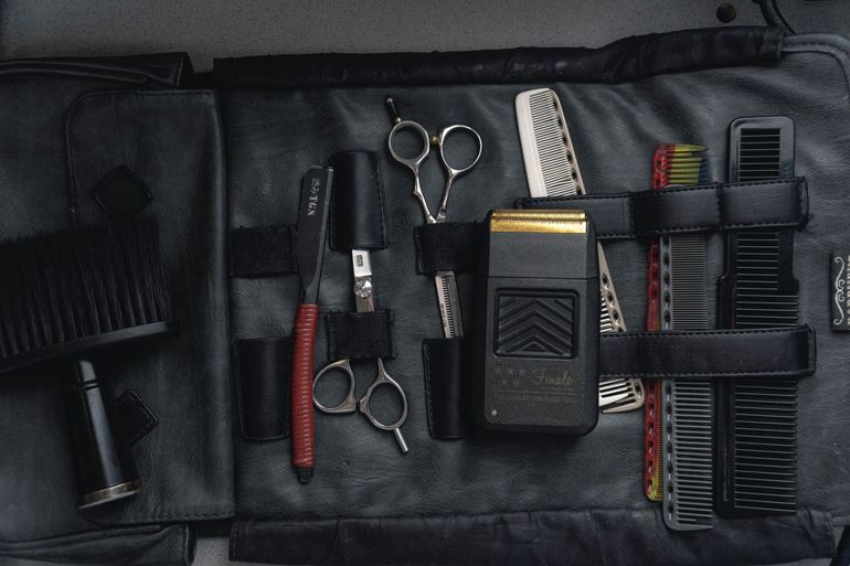 A roll-up leather kit containing professional barber tools, including scissors, combs, a straight razor, and an electric shaver.