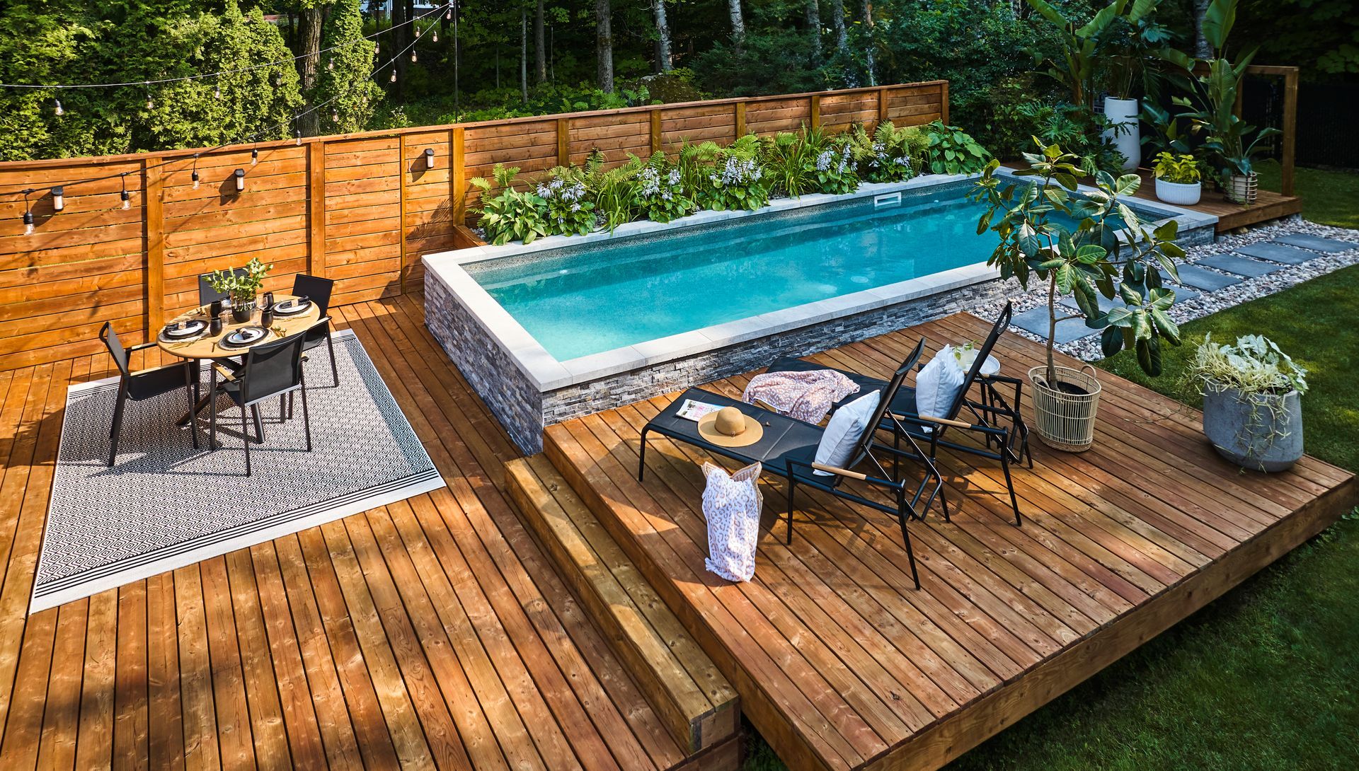 A swimming pool with a waterfall, next to a house with a fence, against a sunset sky.