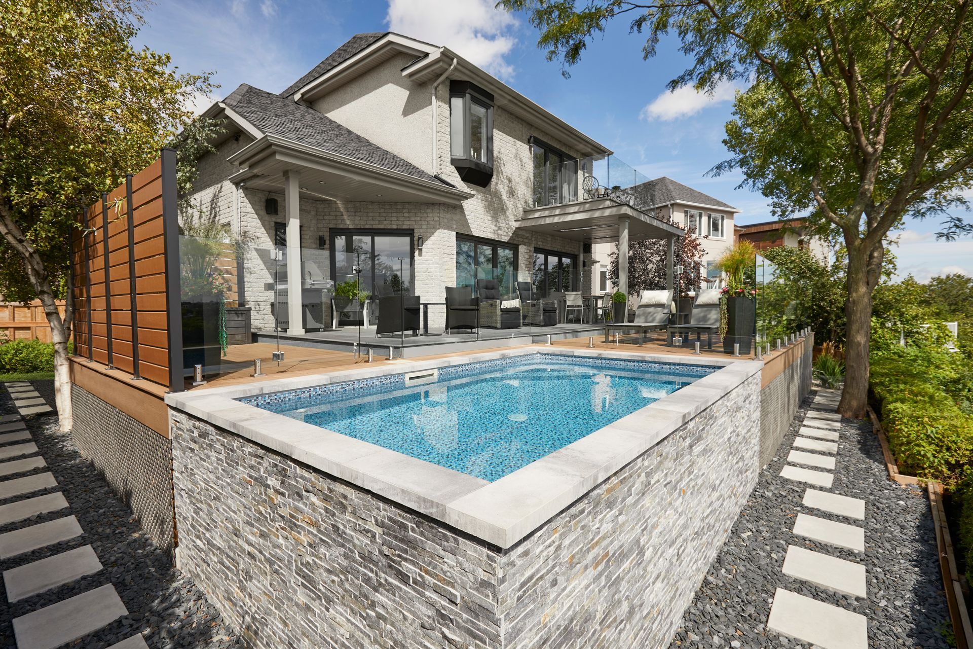 Outdoor patio with pool: gray sofa, hanging chair, fire pit, wood deck, and pool with steps.