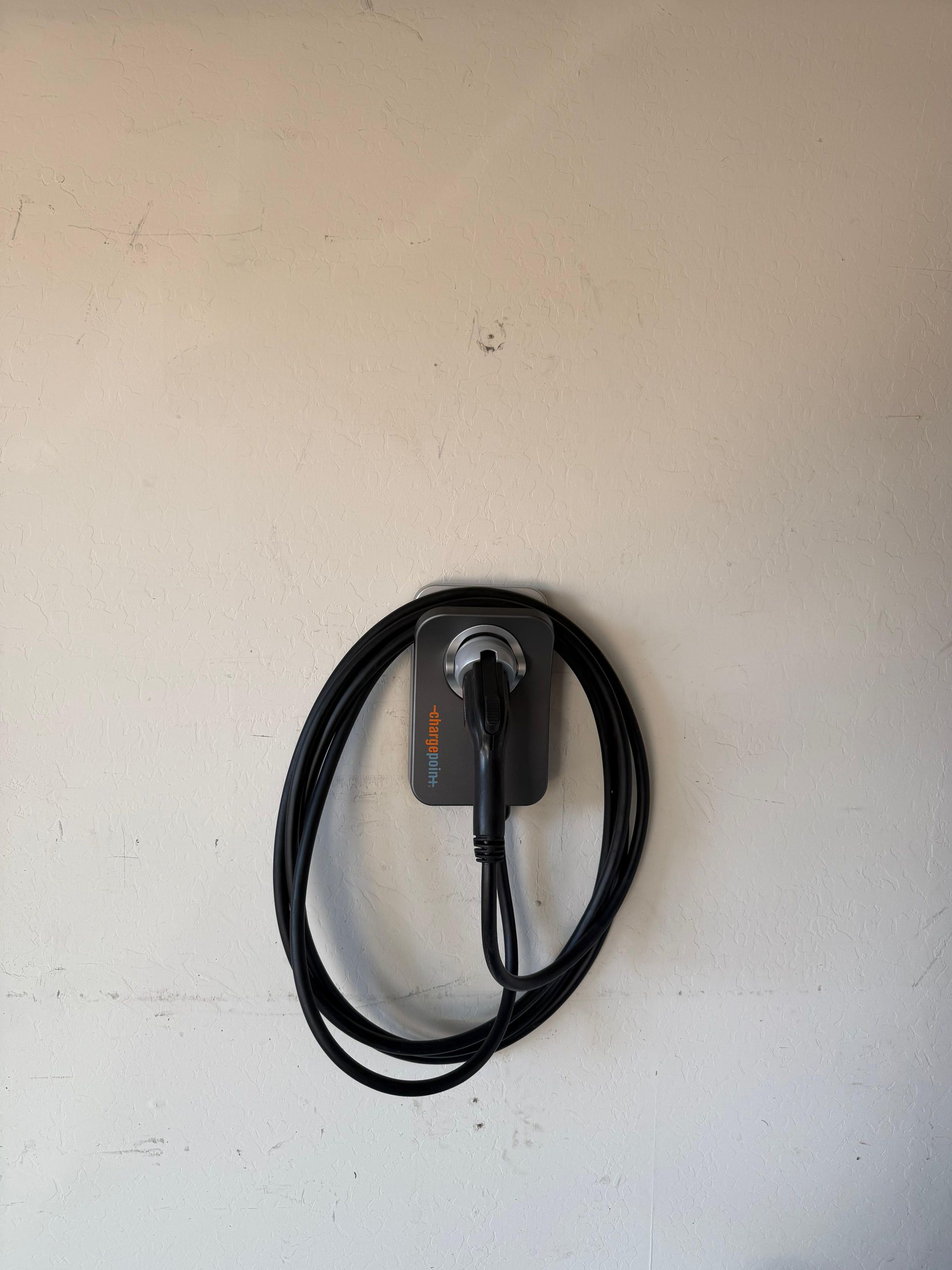 Coiled black charging cable hanging on a wall-mounted outlet or charger.