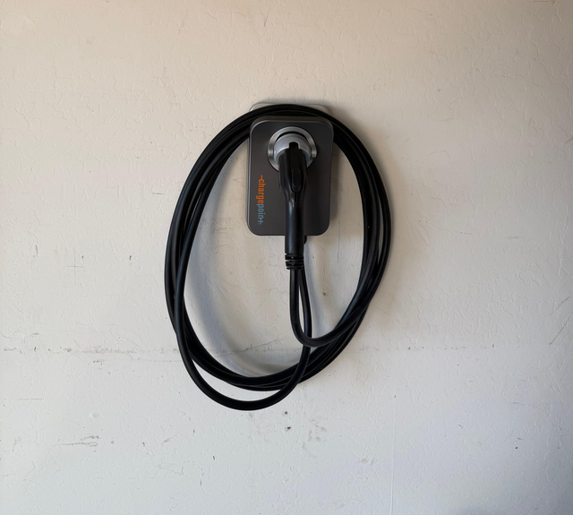 Black EV charging cable coiled on a wall-mounted charger against a white wall.