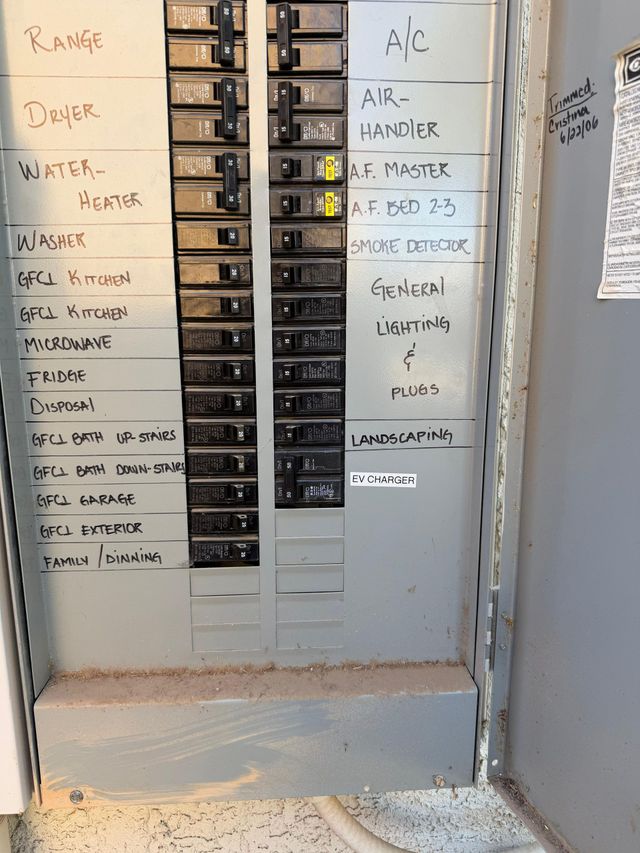 Open electrical breaker panel with handwritten circuit labels on both sides