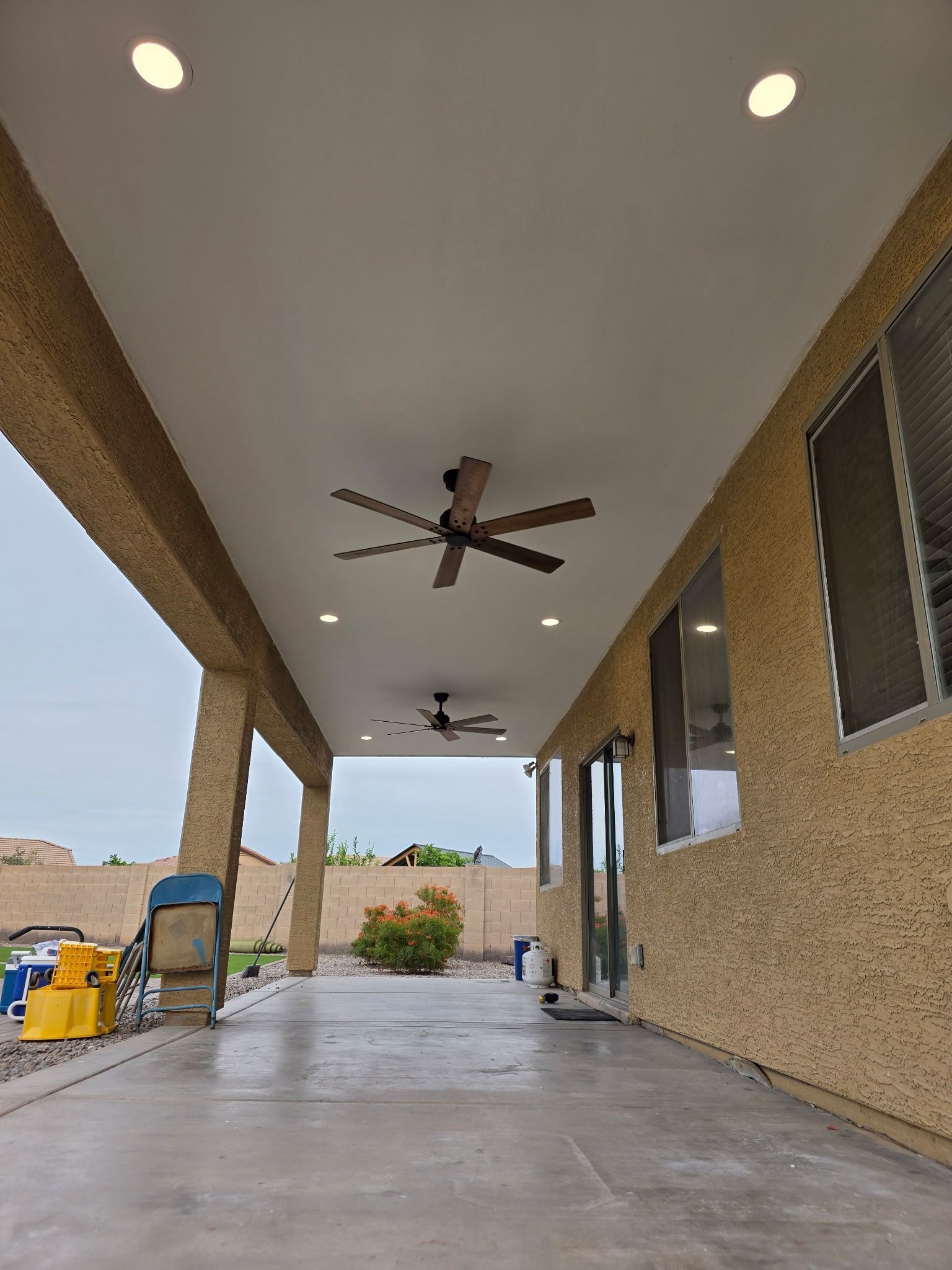 Covered patio with ceiling fans, recessed lights, and a concrete floor beside a tan stucco house.