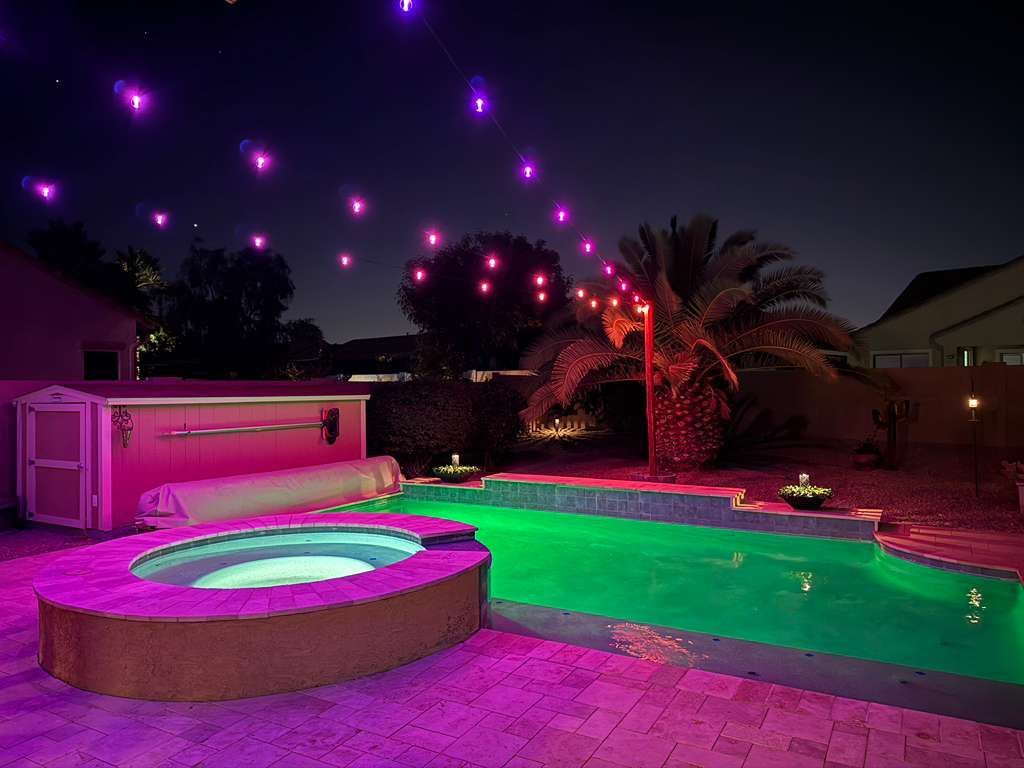 Nighttime backyard with lit pool, and purple-green ambient outdoor lighting.
