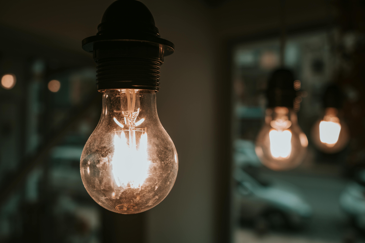 Warm glowing light bulb in a dim room, with blurred bulbs in the background.