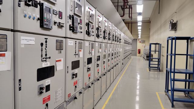 Industrial electrical control room with rows of white control panels and blue storage carts along a clean aisle