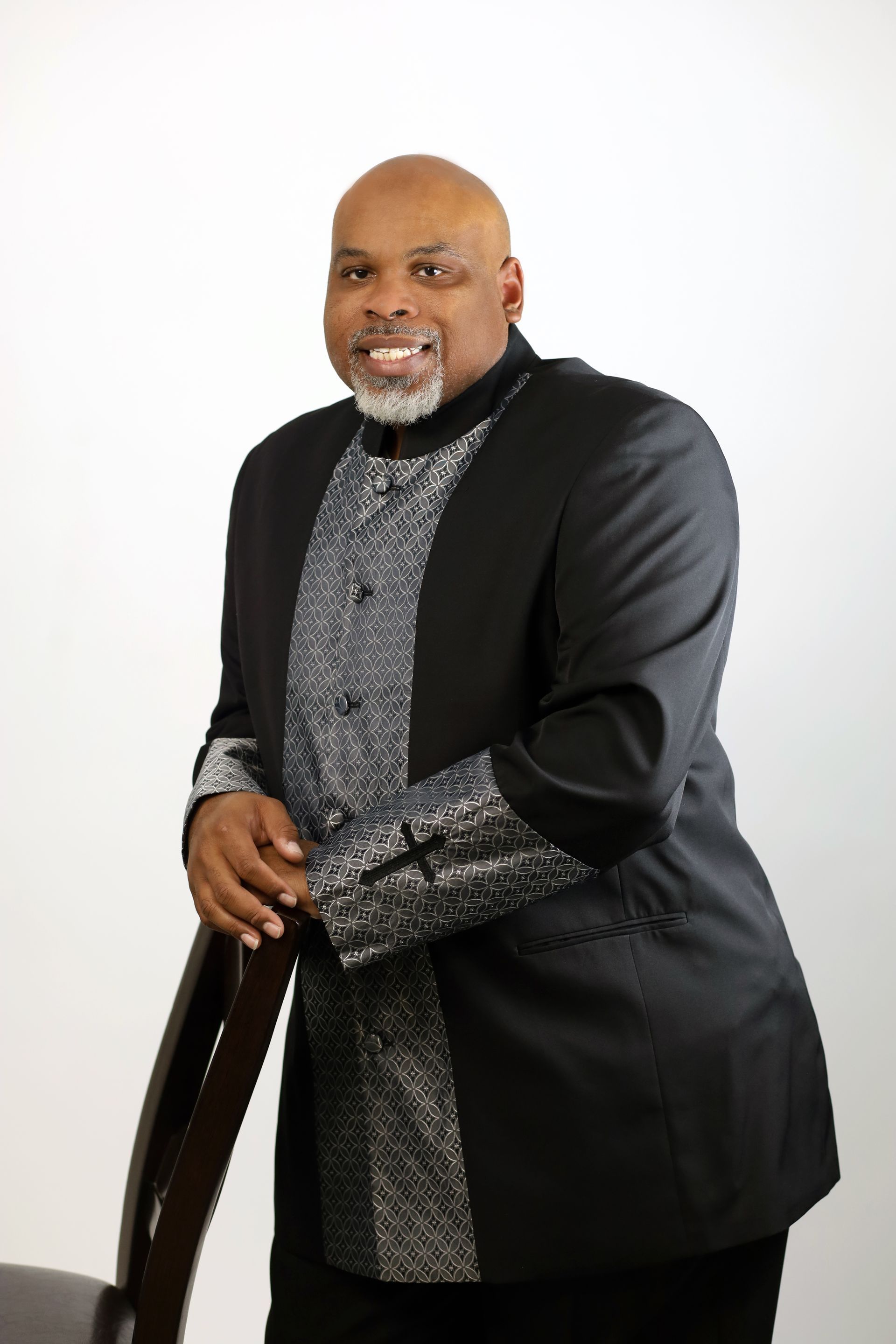 A man in a tuxedo is standing next to a chair.