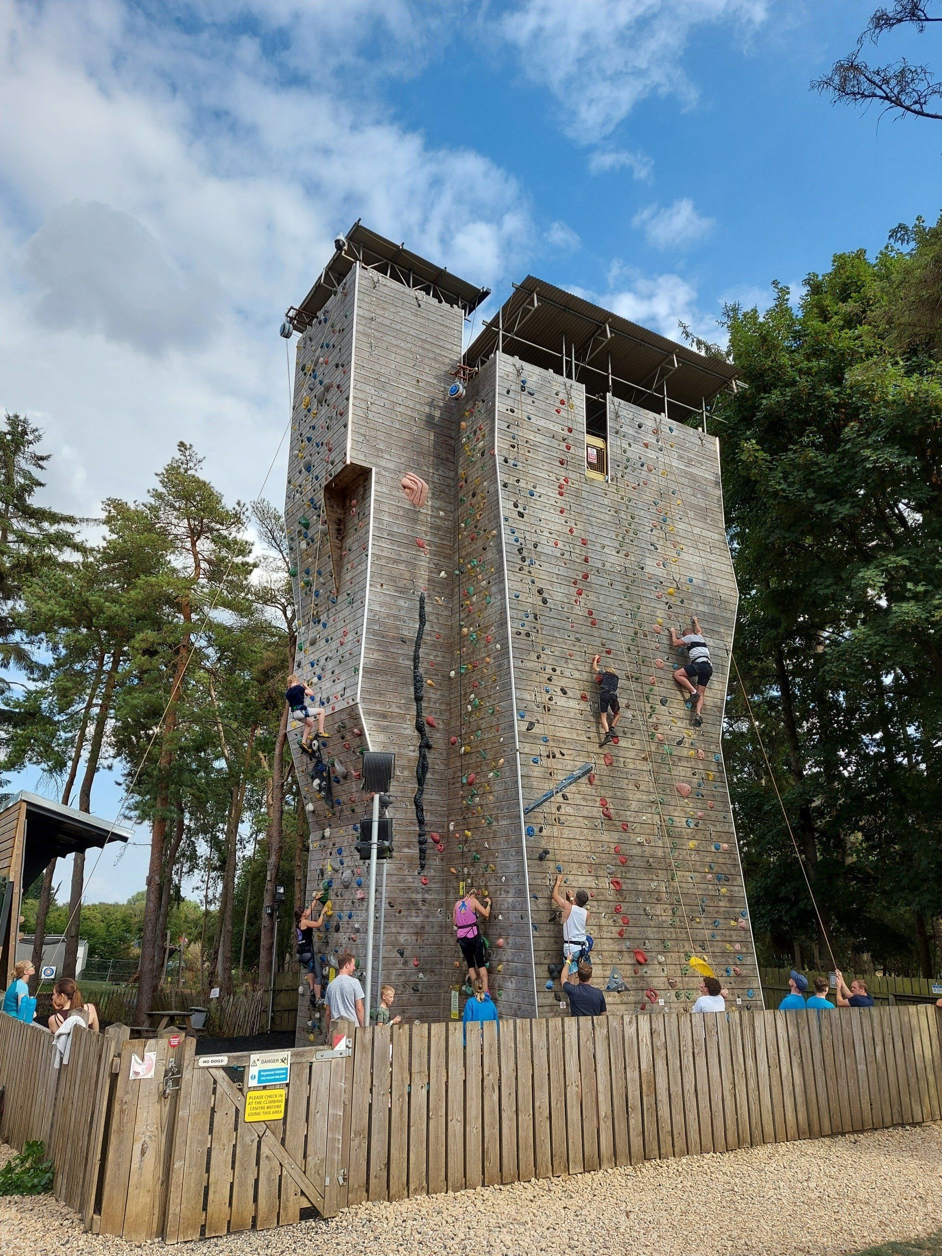 A group of people are climbing a climbing wall behind a wooden fence.
