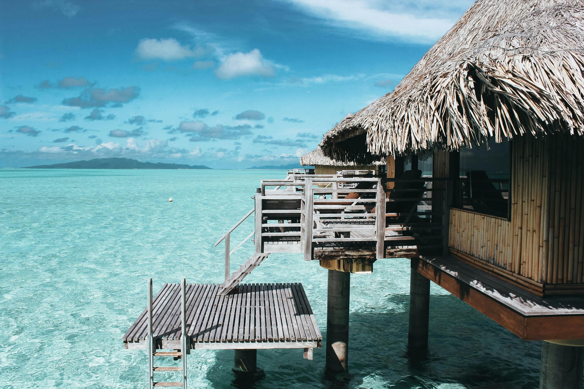 A hut with a thatched roof is in the middle of the ocean.
