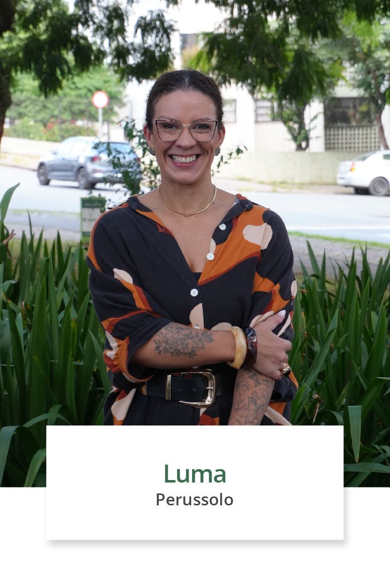 Uma mulher está sentada à mesa com a mão no queixo e sorrindo.