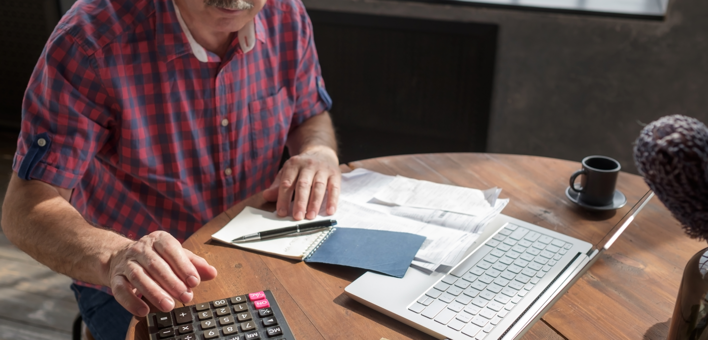 um homem está sentado a uma mesa usando uma calculadora e um laptop.