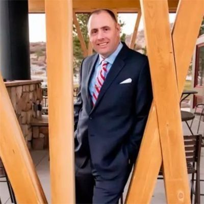 A man in a suit and tie is leaning against a wooden structure