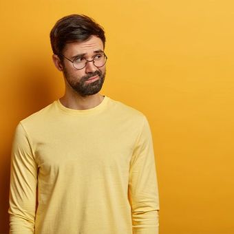 A man wearing glasses and a yellow shirt is standing in front of a yellow wall.