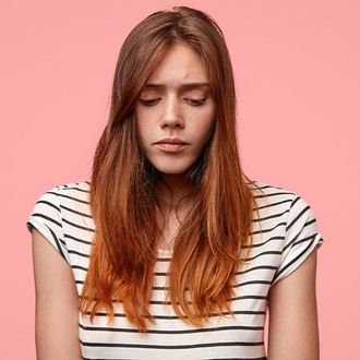 A young woman with long red hair is wearing a striped shirt and looking like she is struggling with stressed thoughts