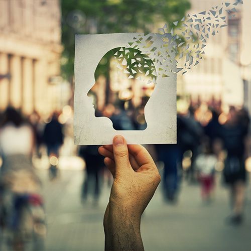 A hand is holding a piece of paper with a silhouette of a head on it with fluttering thoughts