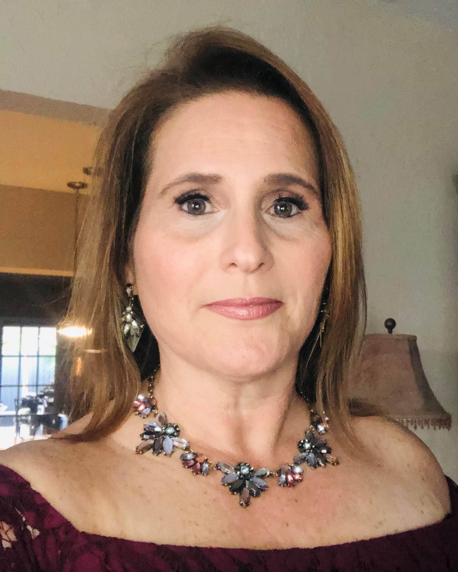 Woman in gray blazer smiling at the camera, wearing a silver necklace and earrings.