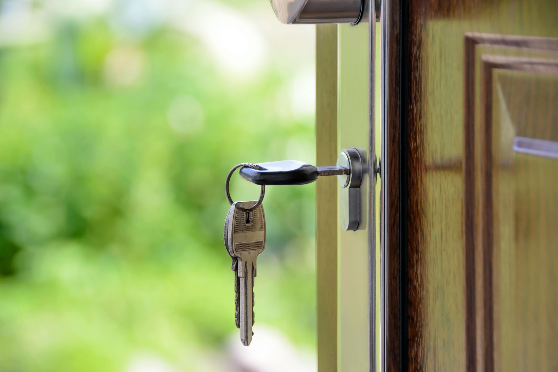 Keys in a door lock, partially open door, blurred green background.