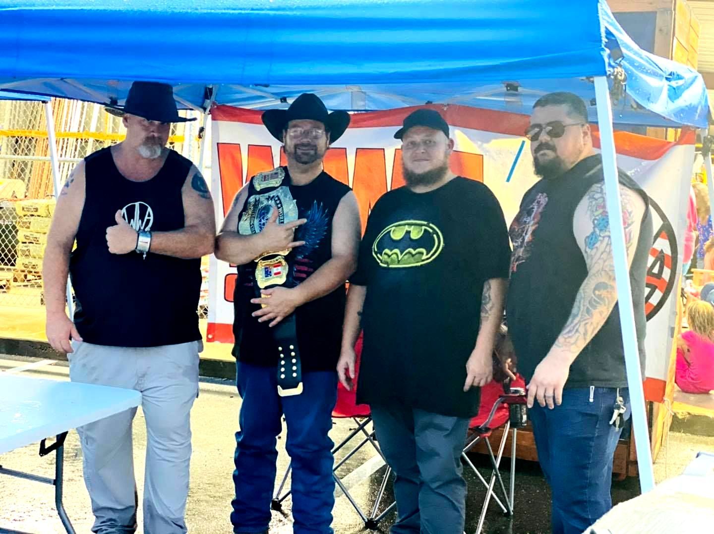 A group of men are standing under a blue tent.